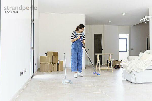 Mid adult woman sweeping living room floor at new home