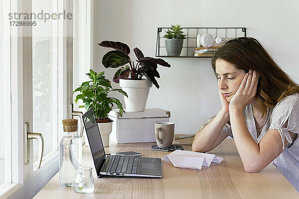 Müde Frau mit auf den Armen ruhendem Kopf im Büro zu Hause