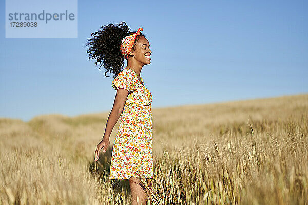 Glückliche junge Frau steht in einem Weizenfeld vor blauem Himmel