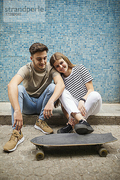 Lächelndes Paar mit Skateboard auf dem Fußweg sitzend