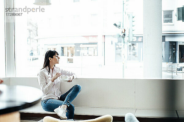 Unternehmerin sitzt mit Kaffeetasse am Fenster eines Cafés