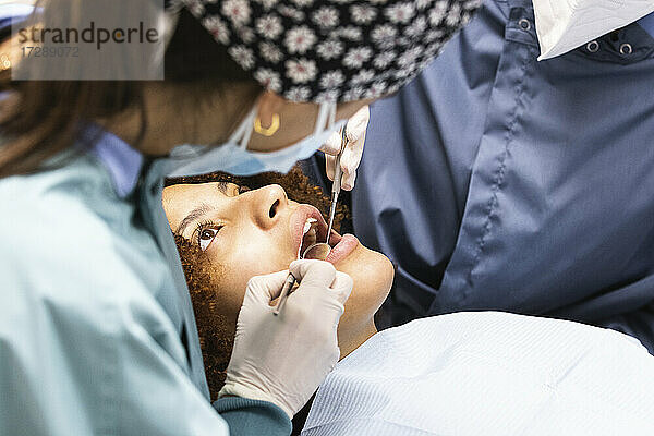 Eine Zahnärztin kontrolliert mit einem Kollegen die Zähne eines Patienten in der Klinik während der Pandemie
