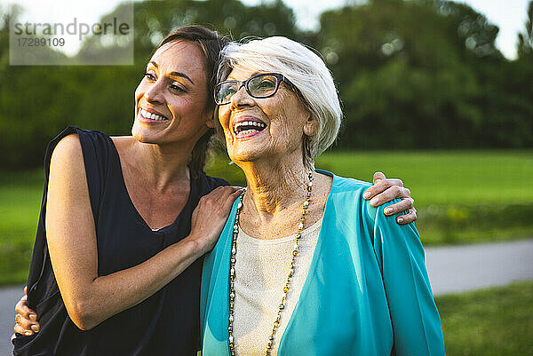 Enkelin lächelt  während sie mit dem Arm um ihre Großmutter im Park steht