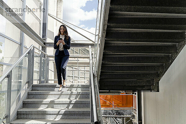 Geschäftsfrau  die ein Smartphone benutzt  während sie eine Treppe in einem Gebäude hinuntergeht