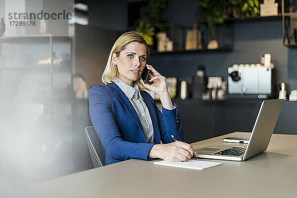 Blonde Frau spricht mit ihrem Smartphone  während sie am Schreibtisch im Büro sitzt