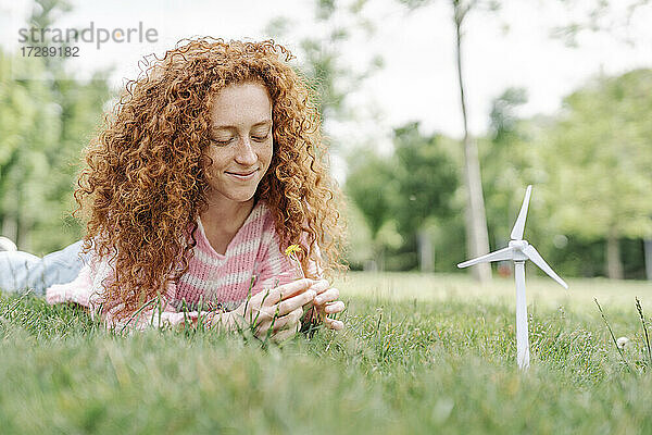 Lächelnde junge Frau mit lockigem Haar  die im Park im Gras liegt