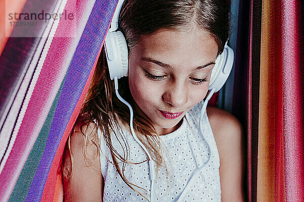 Lächelndes Mädchen hört Musik und entspannt sich in einer mehrfarbigen Hängematte