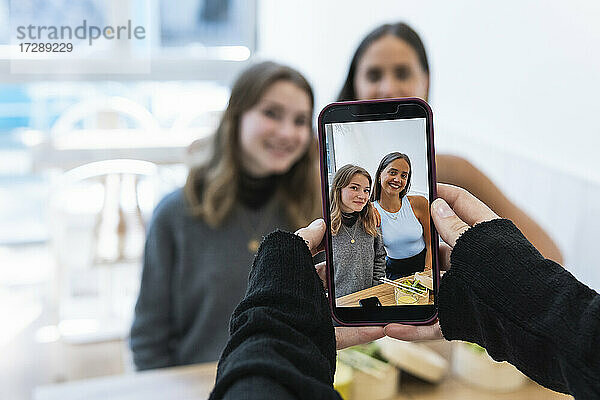 Älterer Mann fotografiert Freundinnen mit dem Handy im Restaurant