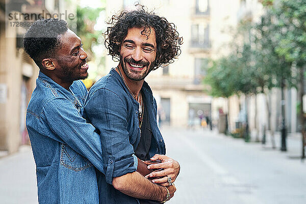 Glücklicher schwuler Mann umarmt männlichen Freund von hinten auf der Straße