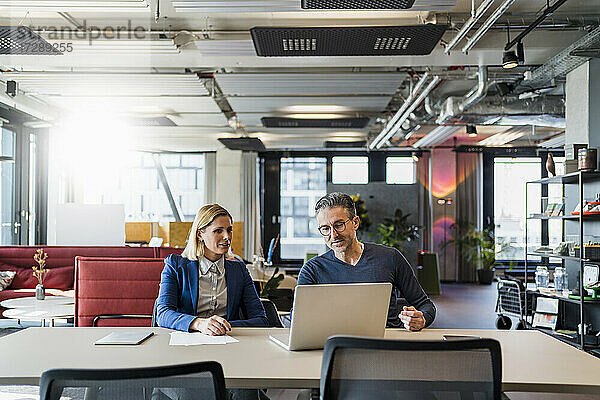 Männliche und weibliche Mitarbeiter diskutieren über den Laptop  während sie am Schreibtisch im Kreativbüro sitzen