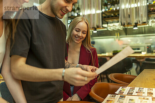 Lächelnde männliche und weibliche Freunde beim Lesen der Speisekarte an einer Bar