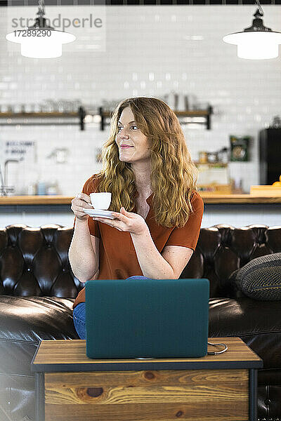 Geschäftsfrau trinkt Kaffee  während sie in der Büro-Cafeteria vor ihrem Laptop sitzt