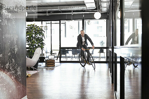 Männlicher Unternehmer fährt Fahrrad im Büro