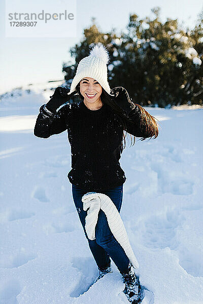 Lächelnde Frau mit Strickmütze  die sich im Schnee vergnügt