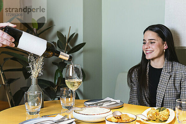 Männlicher Kellner  der einer lächelnden Geschäftsfrau im Restaurant ein Getränk im Weinglas serviert