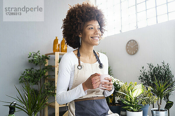 Weibliche Ladenbesitzerin mit Kaffeetasse  die lächelnd in ein Pflanzengeschäft blickt