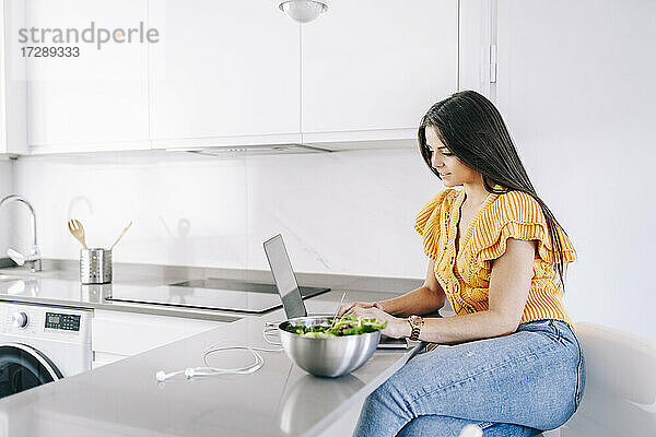 Freiberufliche Mitarbeiterin arbeitet zu Hause an einem Laptop neben einer Salatschüssel