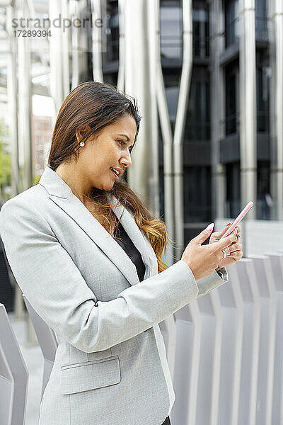 Eine Unternehmerin benutzt ein Mobiltelefon  während sie an einem Geländer steht