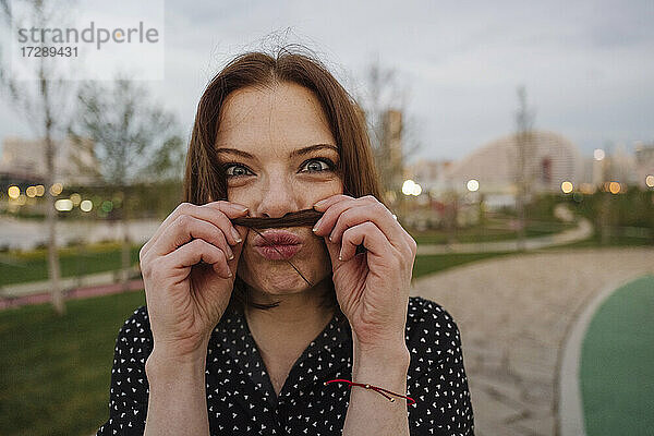 Verspielte reife Frau macht Schnurrbart mit Haaren im Park