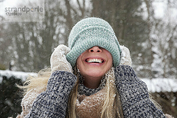 Fröhliche Frau bedeckt ihr Gesicht mit einer Strickmütze im Winter