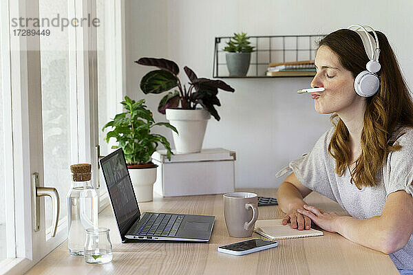 Sorglose Geschäftsfrau  die während eines Videogesprächs im Büro zu Hause einen Stift auf dem Mund balanciert