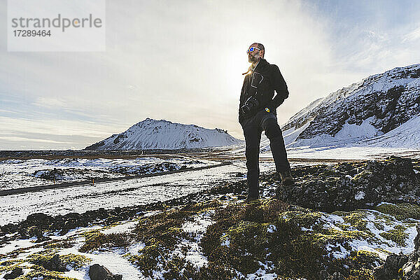 Älterer Mann steht vor einem mit Schnee bedeckten Berg an einem sonnigen Tag