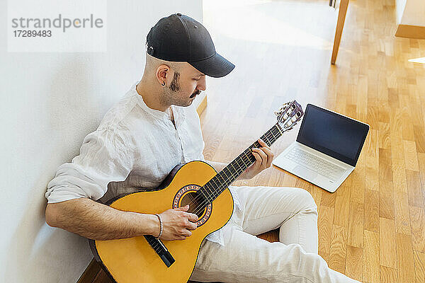 Mann mit Mütze spielt Gitarre  während er zu Hause auf dem Boden sitzt