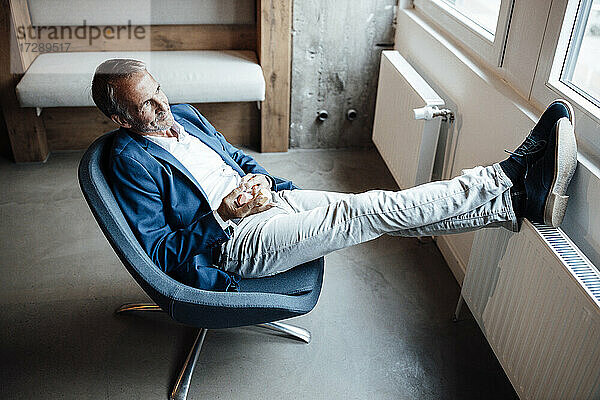Älterer Geschäftsmann hält einen hölzernen Stein  während er sich auf einem Stuhl im Büro entspannt