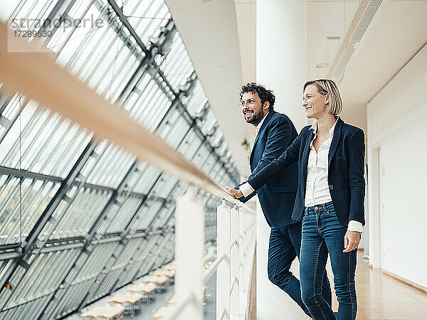 Lächelnde männliche und weibliche Unternehmer schauen weg  während sie sich auf ein Geländer stützen