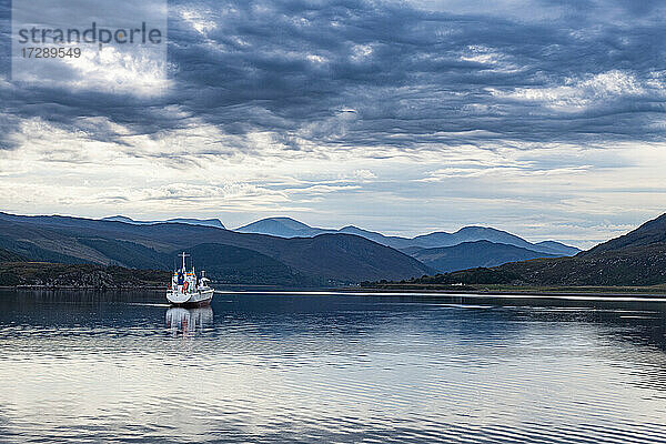 UK  Schottland  Ullapool  Wolken über einem einsamen Fischerboot  das über die Bucht in den schottischen Highlands segelt