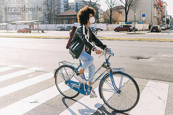 Junge Frau mit Gesichtsmaske und Rucksack auf dem Fahrrad in der Stadt