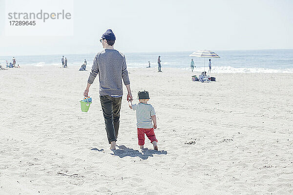 Mann hält die Hand seines Sohnes bei einem Strandspaziergang an einem sonnigen Tag