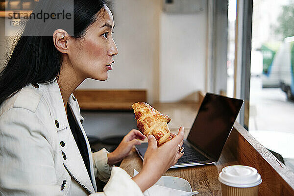 Frau schaut weg  während sie ein Croissant in einem Café isst