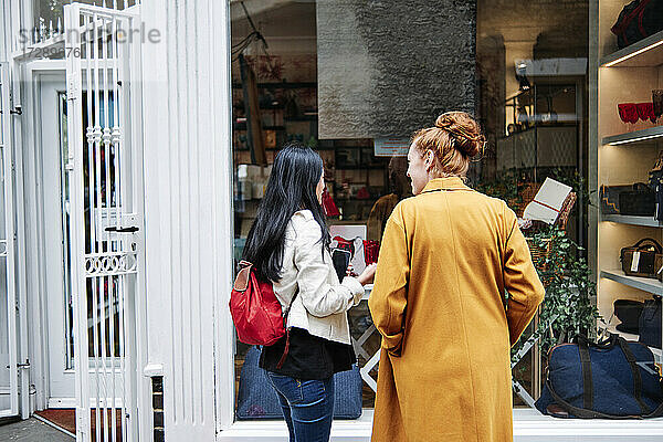 Frau mit Rucksack im Gespräch mit einer Freundin vor einem Kaffeehaus