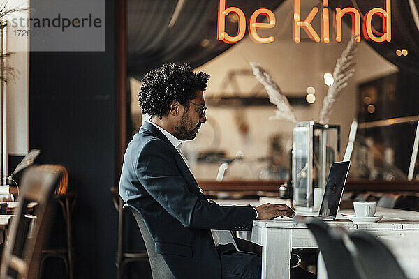 Männlicher Berufstätiger tippt auf einem Laptop  während er in einem Café arbeitet