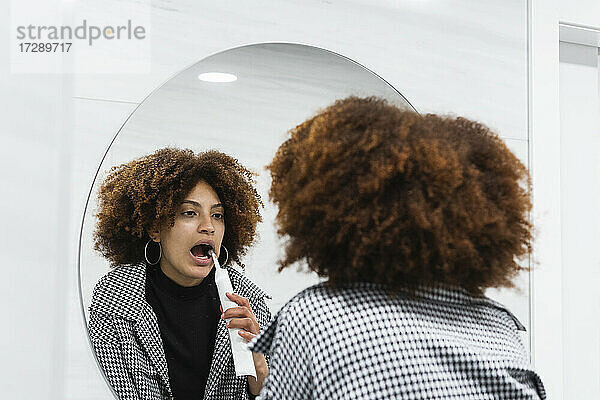 Afro-Patientin beim Zähneputzen im Spiegel auf der Toilette in einer Klinik