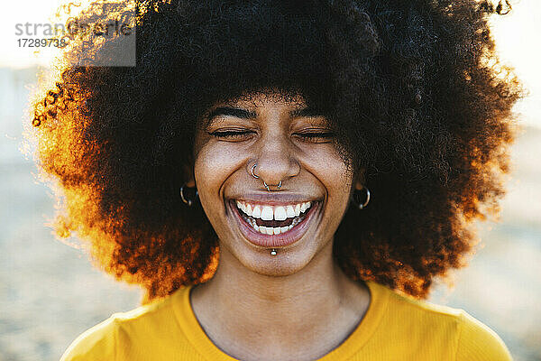 Junge Afro-Frau lachend mit geschlossenen Augen am Strand