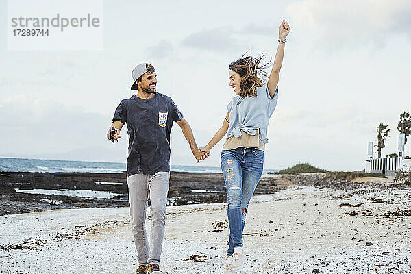 Glückliche Freundin hält die Hand ihres Freundes beim Laufen am Strand