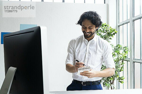 Lächelnder männlicher Unternehmer mit Notizblock und Stift im Büro