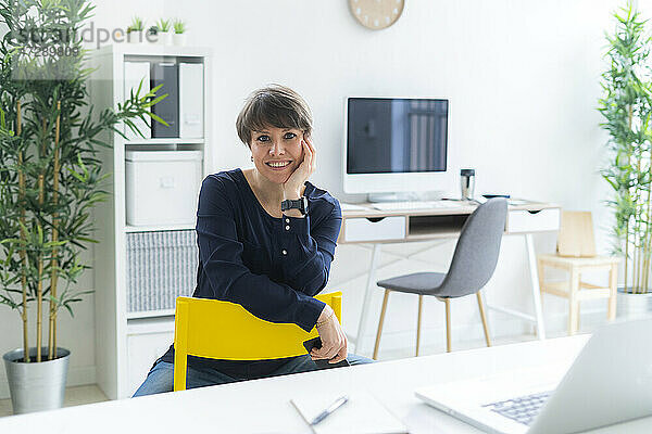 Lächelnde Geschäftsfrau sitzt auf einem Stuhl im Büro