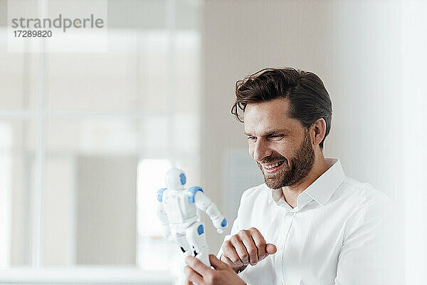 Lächelnder Geschäftsmann hält Robotermodell im Büro
