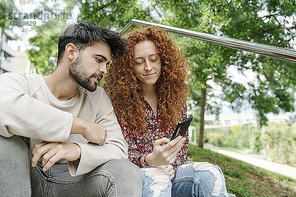 Junges Paar  das im Park gemeinsam ein Smartphone benutzt