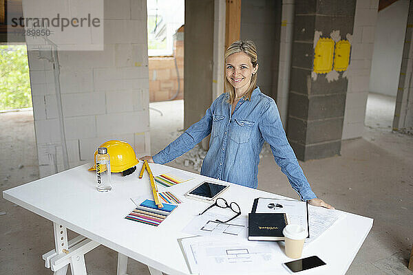 Lächelnde Bauunternehmerin steht am Tisch in einer Wohnung