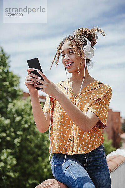 Frau  die ein Selfie mit ihrem Smartphone macht  während sie auf dem Balkon Musik hört