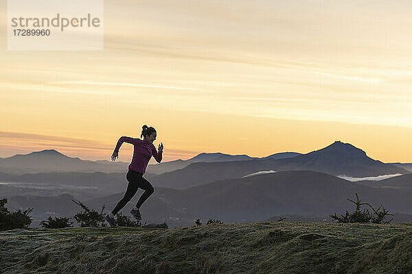 Weibliche Läuferin läuft auf einem Hügel vor dramatischem Himmel