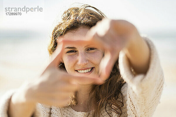 Lächelnde Frau macht Fingerrahmen am Strand während der Ferien