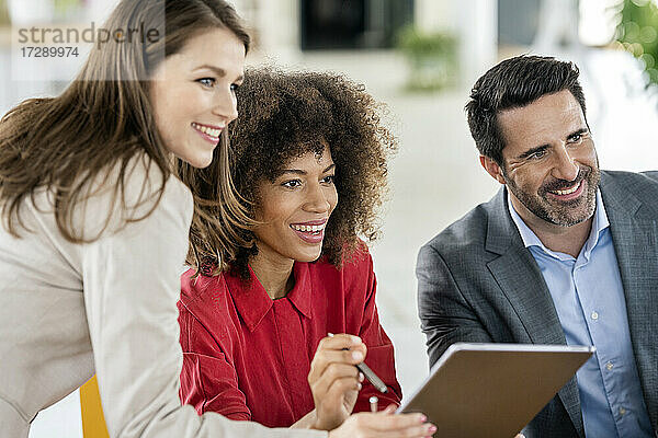 Lächelnde männliche und weibliche Fachkräfte mit Grafiktablett  die im Büro wegschauen