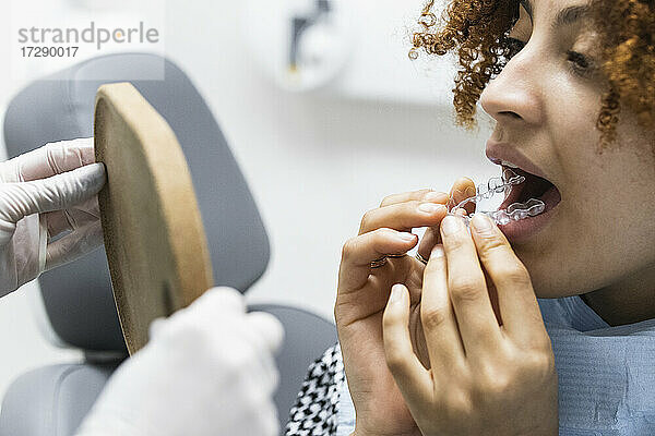 Weiblicher Patient  der eine Zahnschiene trägt  während er in den Spiegel schaut  den der Zahnarzt in der Klinik hält
