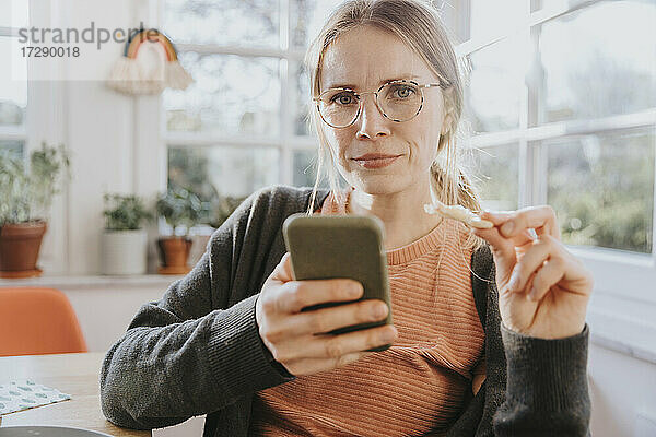 Frau mit Brille starrt  während sie ein Smartphone zu Hause hält