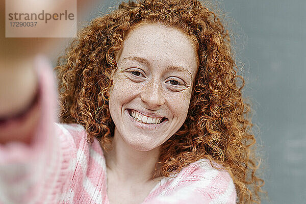 Fröhliche rothaarige Frau mit lockigem Haar lächelnd